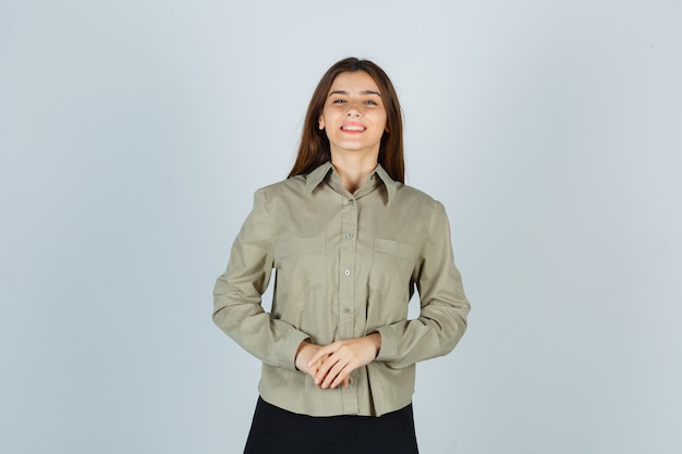 Foto gratuita hembra joven manteniendo las manos delante de ella en camisa, falda y mirando feliz