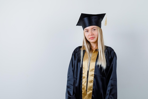 Hembra joven mirando a la cámara en uniforme de posgrado y con aspecto sensato.