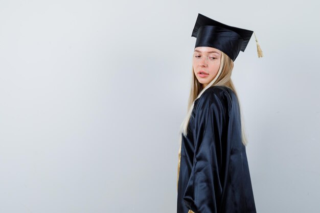 Hembra joven mirando por encima del hombro en uniforme de posgrado y atractivo. .