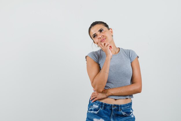 Hembra joven mirando a otro lado en camiseta, pantalones cortos y mirando pensativo