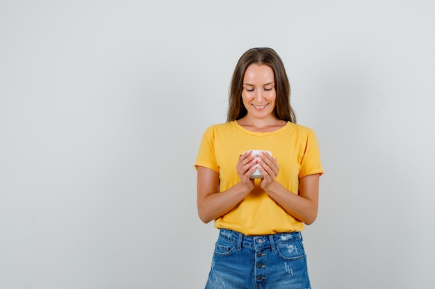 Hembra joven mirando en portalápices y sonriendo en camiseta, pantalones cortos