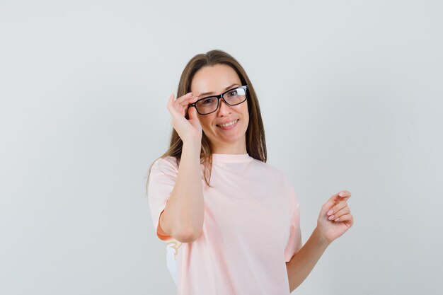 Hembra joven mirando a través de gafas en camiseta rosa y mirando alegre. vista frontal.