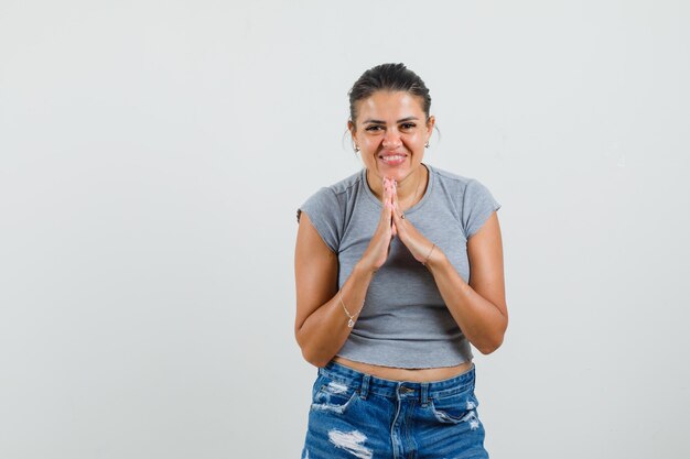 Hembra joven mostrando gesto de namaste en camiseta, pantalones cortos y mirando alegre