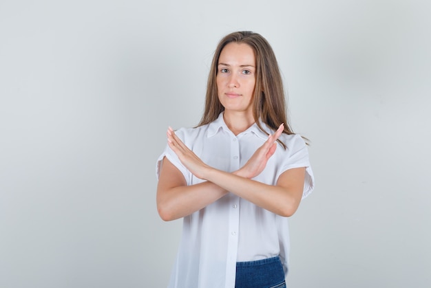 Hembra joven mostrando gesto de parada en camisa blanca, jeans y aspecto cansado