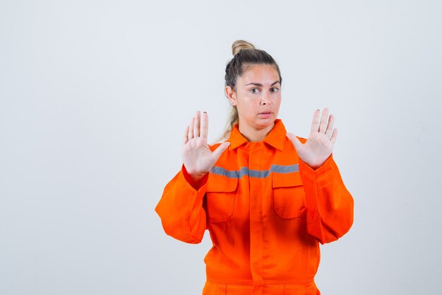 Hembra joven mostrando gesto de parada en uniforme de trabajador y mirando serio. vista frontal.