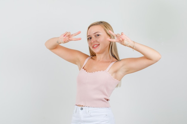 Hembra joven mostrando gesto de paz en camiseta, minifalda y mirando alegre