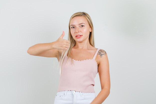 Hembra joven mostrando el pulgar hacia arriba en camiseta, minifalda y mirando complacido