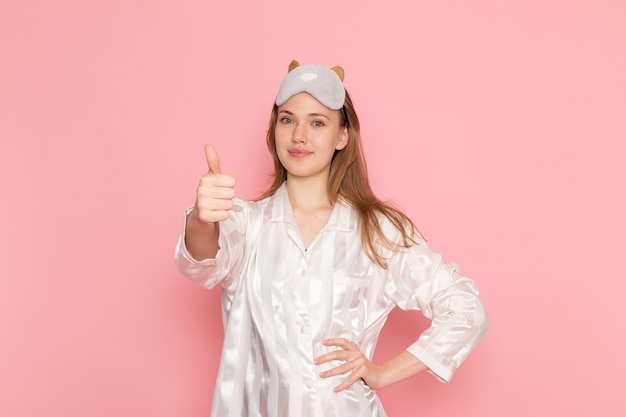 Hembra joven en pijama y antifaz para dormir posando sonriendo en rosa