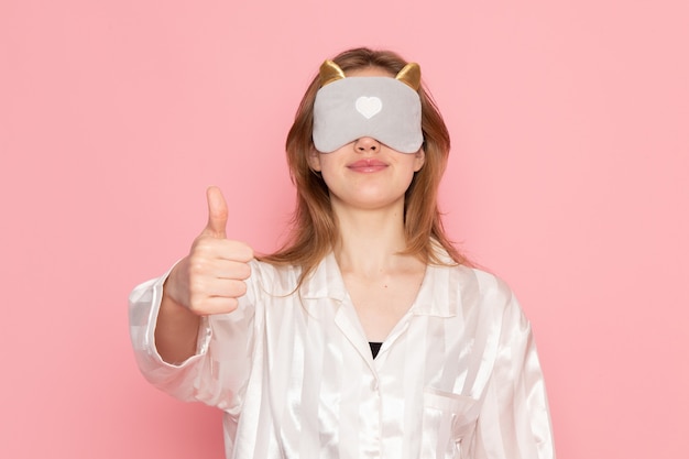 Foto gratuita hembra joven en pijama y antifaz para dormir posando con una sonrisa mostrando como signo en rosa