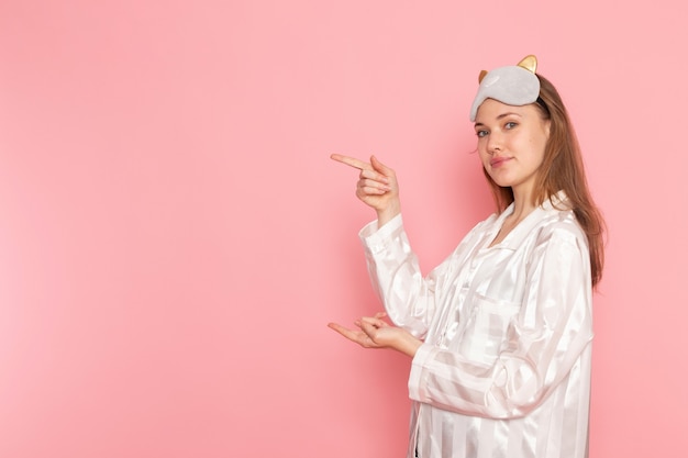 Hembra joven en pijama y antifaz para dormir posando con una sonrisa en rosa