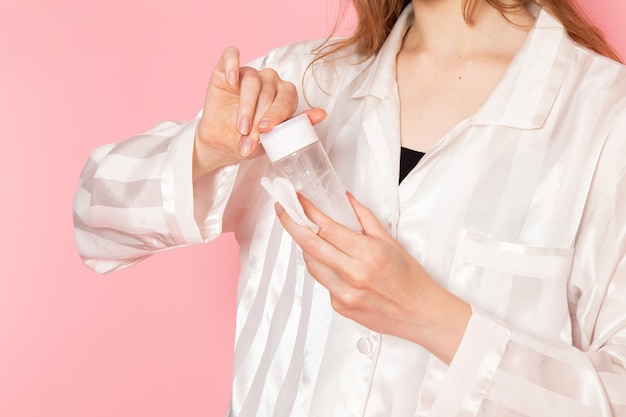 Hembra joven en pijama y antifaz para dormir sosteniendo spray de maquillaje en rosa