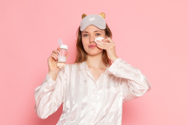 Foto gratuita hembra joven en pijama y antifaz para dormir con spray de maquillaje en rosa