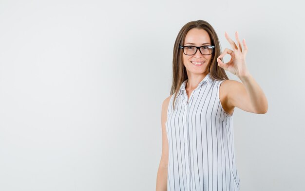 Hembra joven que muestra un gesto aceptable en camiseta y parece feliz. vista frontal.