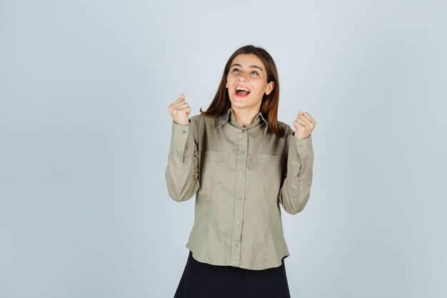 Hembra joven que muestra el gesto del ganador en camisa, falda y mirando dichoso