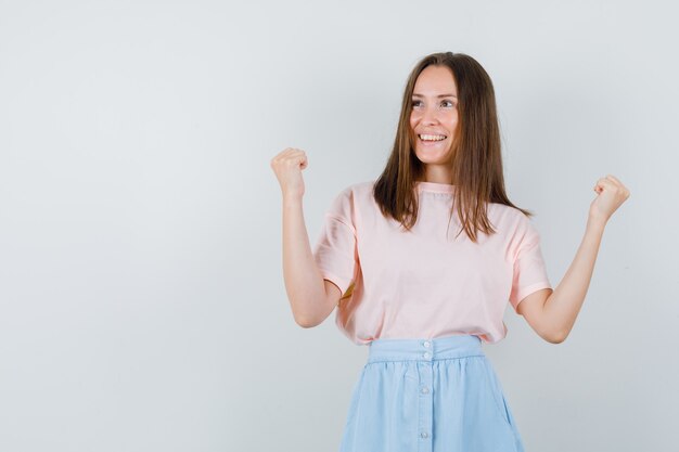 Hembra joven que muestra el gesto del ganador en camiseta, falda y con suerte, vista frontal.