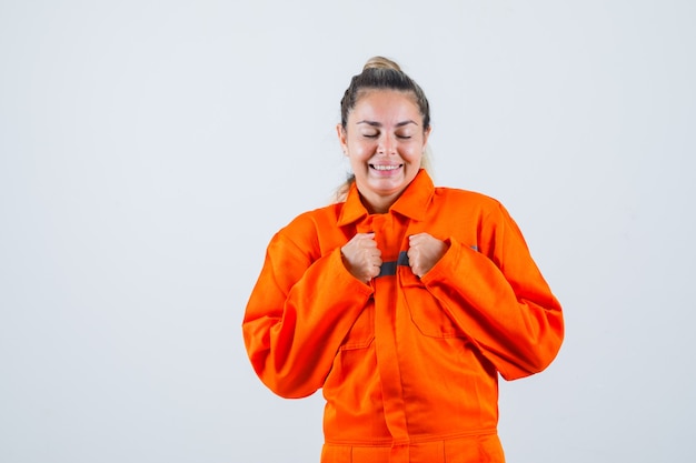 Hembra joven que muestra el gesto del ganador en uniforme del trabajador y parece emocionado. vista frontal.