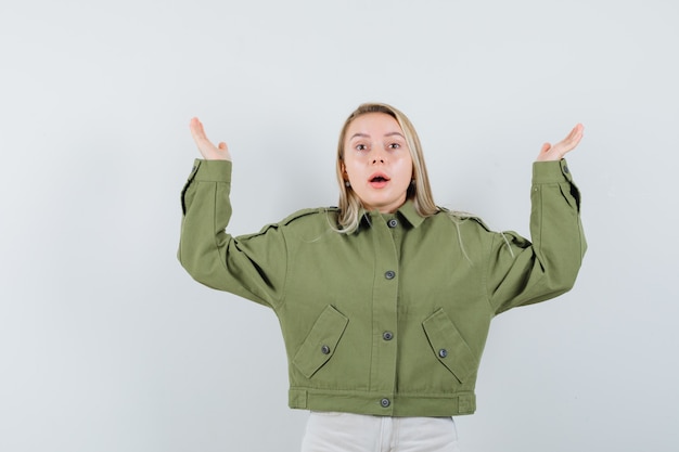 Hembra joven que muestra un gesto de impotencia en chaqueta verde, jeans y aspecto preocupado. vista frontal.