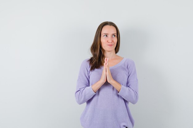 Hembra joven que muestra el gesto de namaste en blusa lila y parece optimista