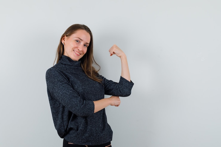 Foto gratuito hembra joven que muestra los músculos del brazo en camisa y parece confiada. vista frontal.