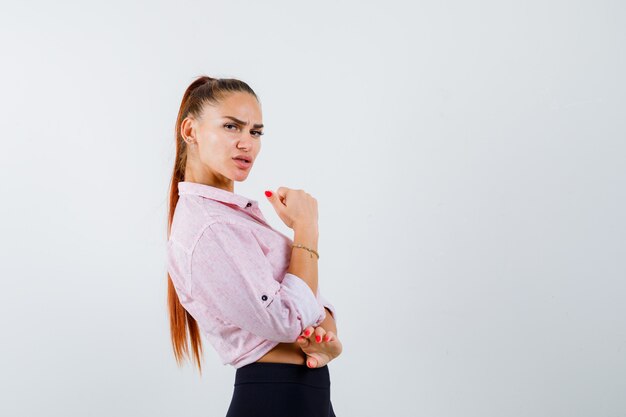 Hembra joven que muestra el pulgar hacia arriba en camisa casual, pantalones y parece seguro. vista frontal.