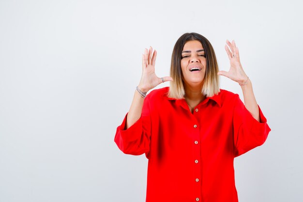 Hembra joven que muestra el signo del tamaño en una camisa roja de gran tamaño y que parece confiada, vista frontal.