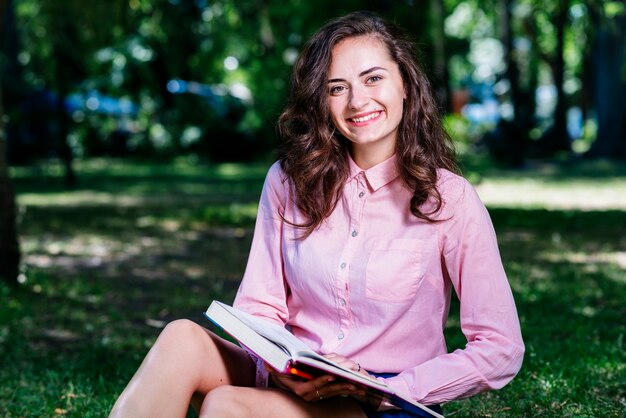 Hembra joven que se sienta en el parque con el libro