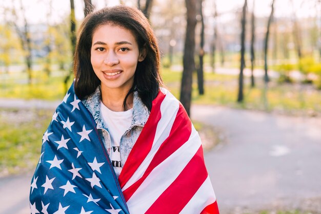 Hembra joven que sostiene la bandera americana en día soleado