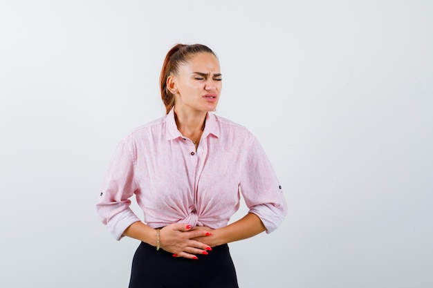 Hembra joven que sufre de dolor de estómago en camisa casual, pantalones y mal aspecto. vista frontal.