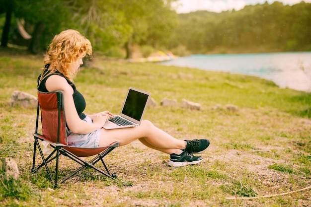 Hembra joven que usa la computadora portátil al aire libre