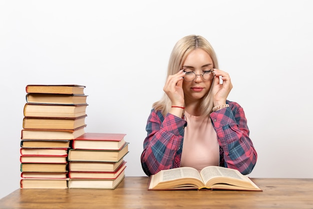 Hembra joven sentada con libros y leyendo en blanco claro