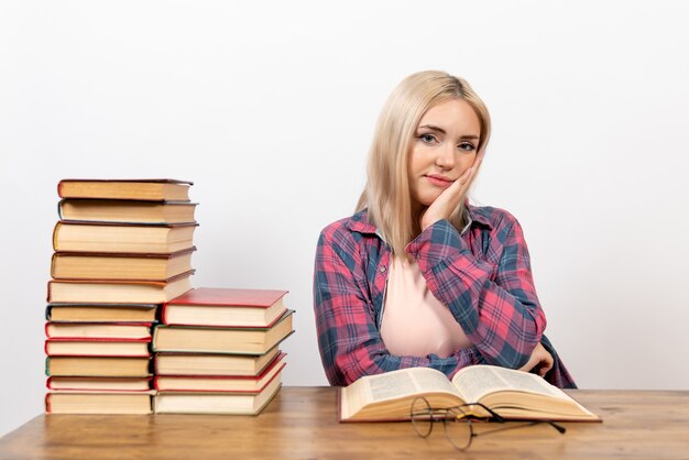 Hembra joven sentada con libros y leyendo en blanco