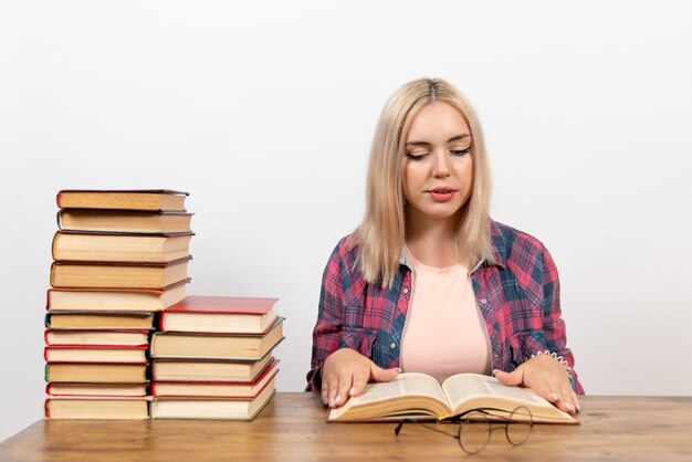 Hembra joven sentada con libros y leyendo en blanco