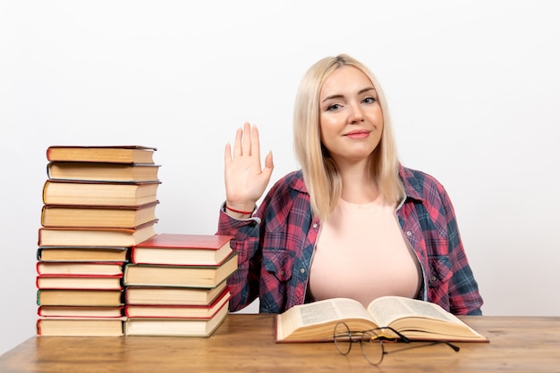 Hembra joven sentada con libros y leyendo en blanco