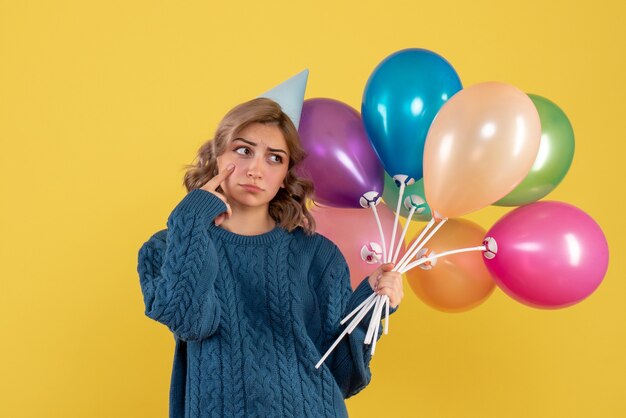 Hembra joven sosteniendo globos de colores detrás de su espalda en amarillo