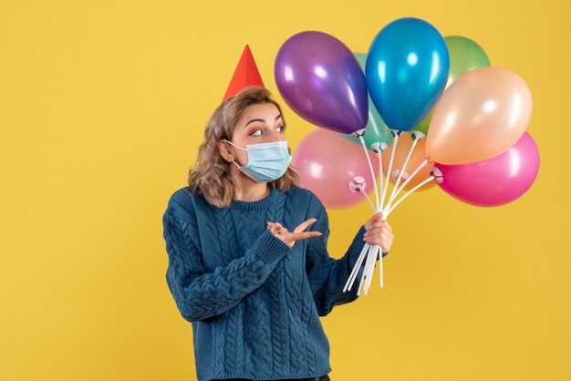 Hembra joven sosteniendo globos de colores en máscara en amarillo