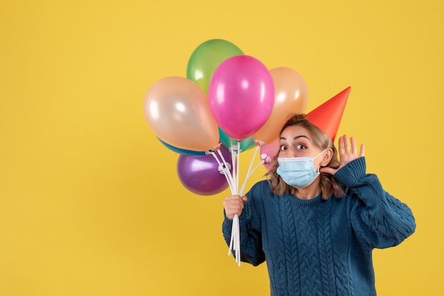 Hembra joven sosteniendo globos de colores en máscara en amarillo