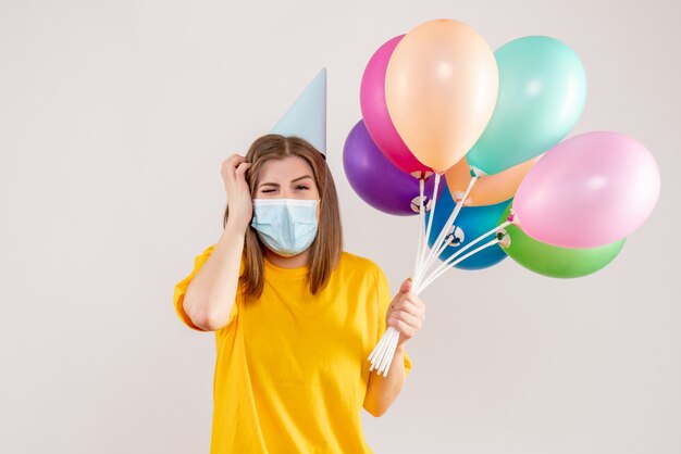 Hembra joven sosteniendo globos de colores en máscara en blanco