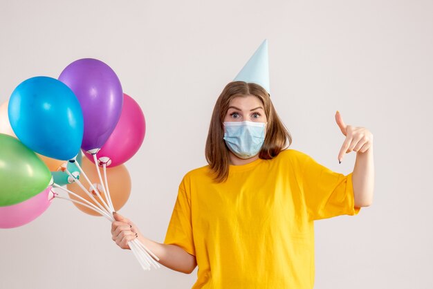 Hembra joven sosteniendo globos de colores en máscara en blanco