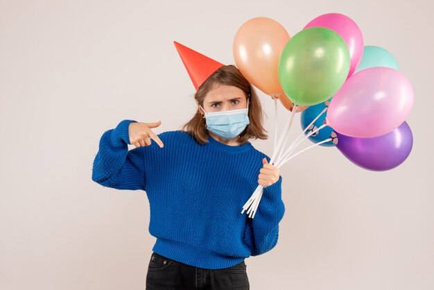 Hembra joven sosteniendo globos de colores en máscara en blanco