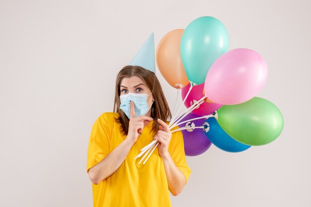 Hembra joven sosteniendo globos de colores en máscara en blanco