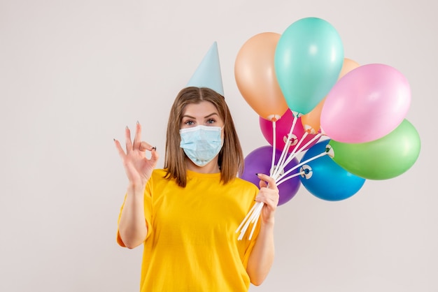 Hembra joven sosteniendo globos de colores en máscara en blanco