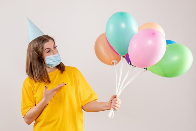 Hembra joven sosteniendo globos de colores en máscara en blanco