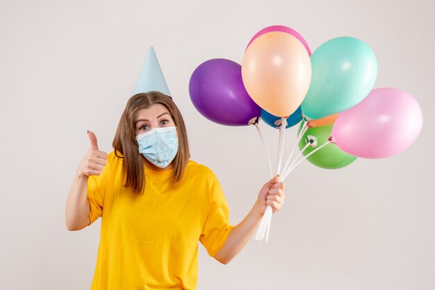 Hembra joven sosteniendo globos de colores en máscara en blanco