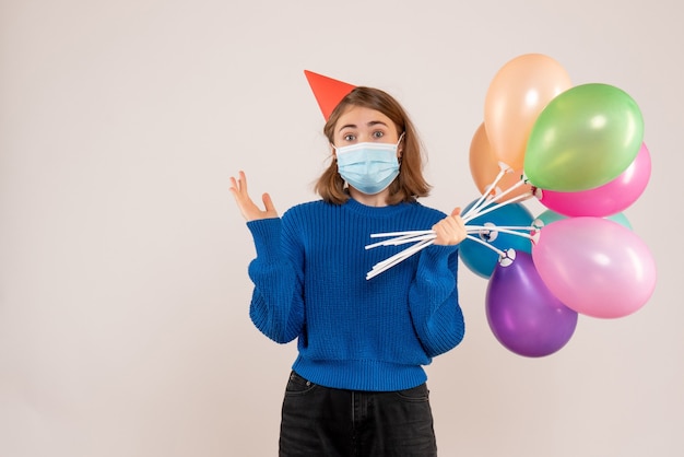 Foto gratuita hembra joven sosteniendo globos de colores en máscara en blanco