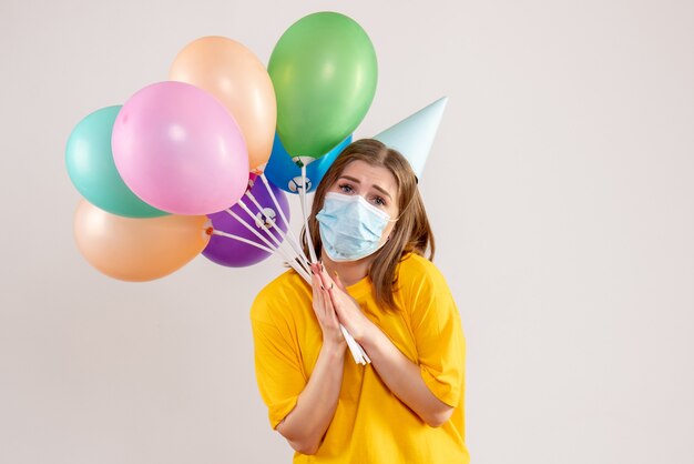 Hembra joven sosteniendo globos de colores en máscara estéril en blanco