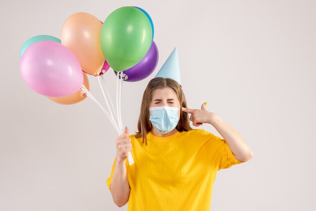 Hembra joven sosteniendo globos de colores en máscara estéril en blanco