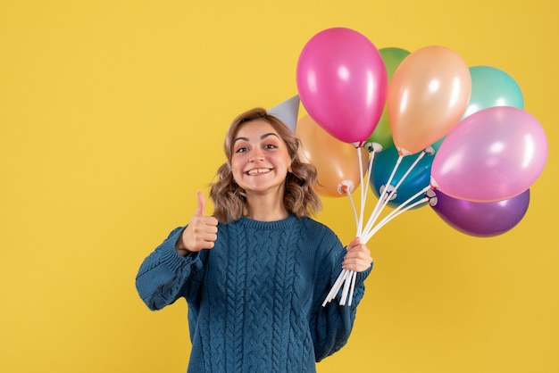 Hembra joven sosteniendo globos de colores sobre amarillo