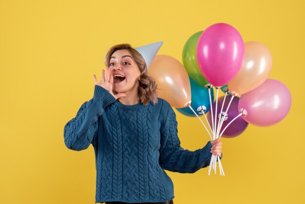 Hembra joven sosteniendo globos de colores sobre amarillo