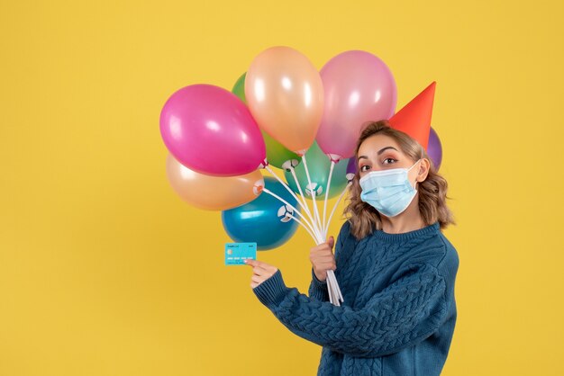 Hembra joven sosteniendo globos de colores y tarjeta bancaria en amarillo