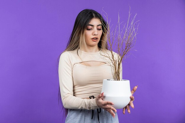 Hembra joven sosteniendo maceta seca y se para sobre fondo púrpura Foto de alta calidad